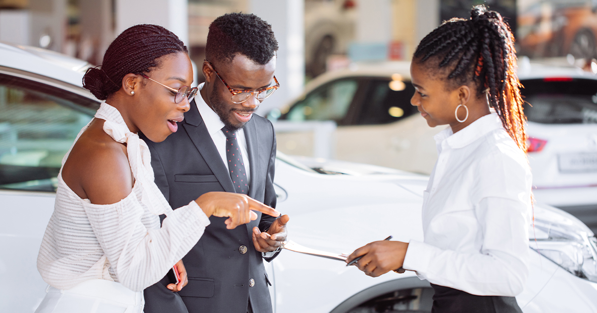 A salesperson at a car dealership showing a couple available vehicle offers