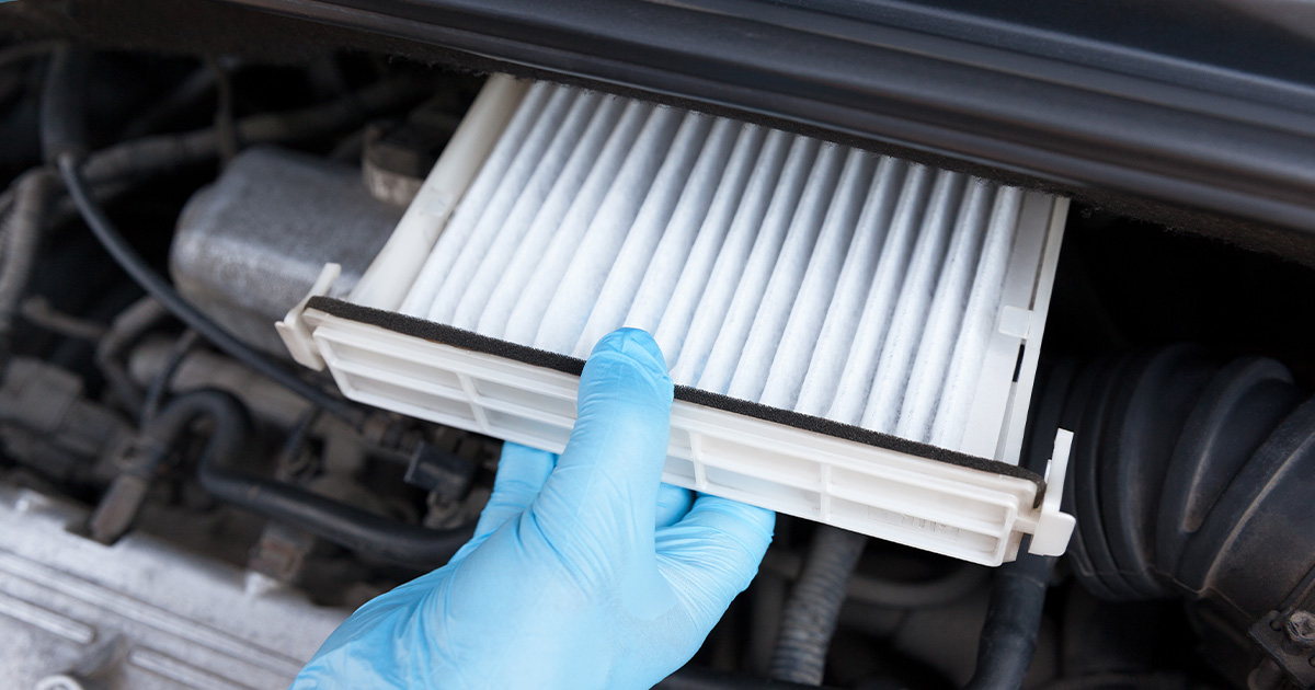 Close-up of a service technician replacing a vehicle's cabin air filter with a new filter.