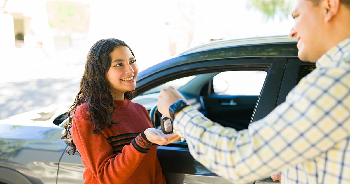 A car salesperson at the dealership handing a new car owner their keys